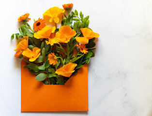 Various orange flowers in an open orange mail envelope on a marble pastel background. Flat lay. Copy space. Minimalistic composition. Concept of love and nature