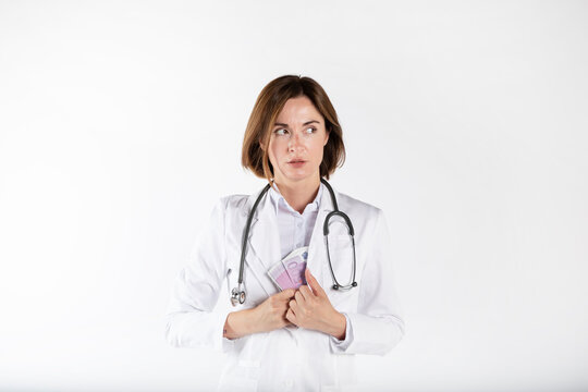 Close-up photo of cunning female doctor hiding pack of cash money in her medical gown isolated on white background. Bribe concept