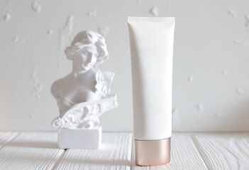 Cosmetic cream bottle and head statue on table, mockup