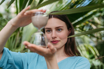 Young woman with hourglass in jungle, concept of nature protection.