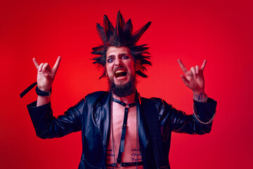 Aggressive impressive pose. Rok musician, man posing with hand gesture on rock against red studio...