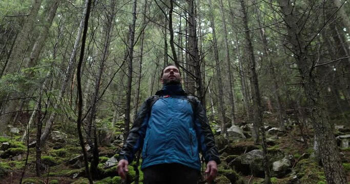 Portrait of a man with a backpack standing in the rain in the forest and raising his hands to the mountain breathing in the mountain air and meditating. The man is alone in the mountains. Hiking among