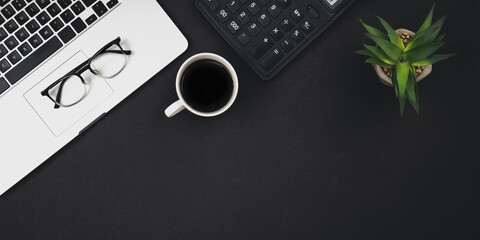 Flat lay black background with laptop, coffee cup and calculator, top view.