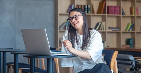 Cheerful young woman in glasses in front of a laptop.