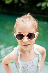 Smiling cute little girl in sunglasses in pool in sunny day.