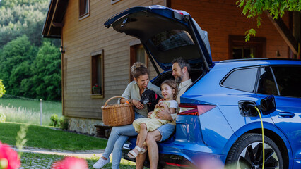Happy family sitting in a car trunk and waiting for charging.