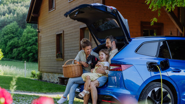 Happy Family Sitting In A Car Trunk And Waiting For Charging.