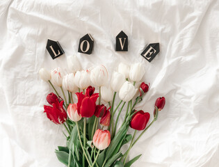 Decorative word Love and tulips in a white bed, top view.