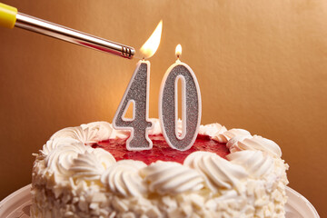 A candle in the form of the number 40, stuck in a festive cake, is lit. Celebrating a birthday or a...