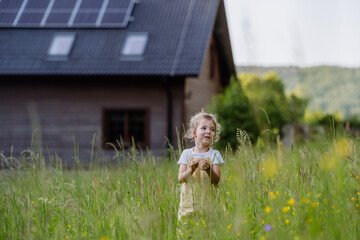 Portrait of little girl in front of family house with solar panels, concept of sustainable...