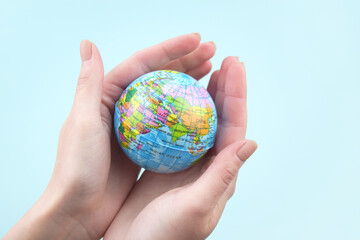Women's hands hold a globe in their hands on a light blue background.