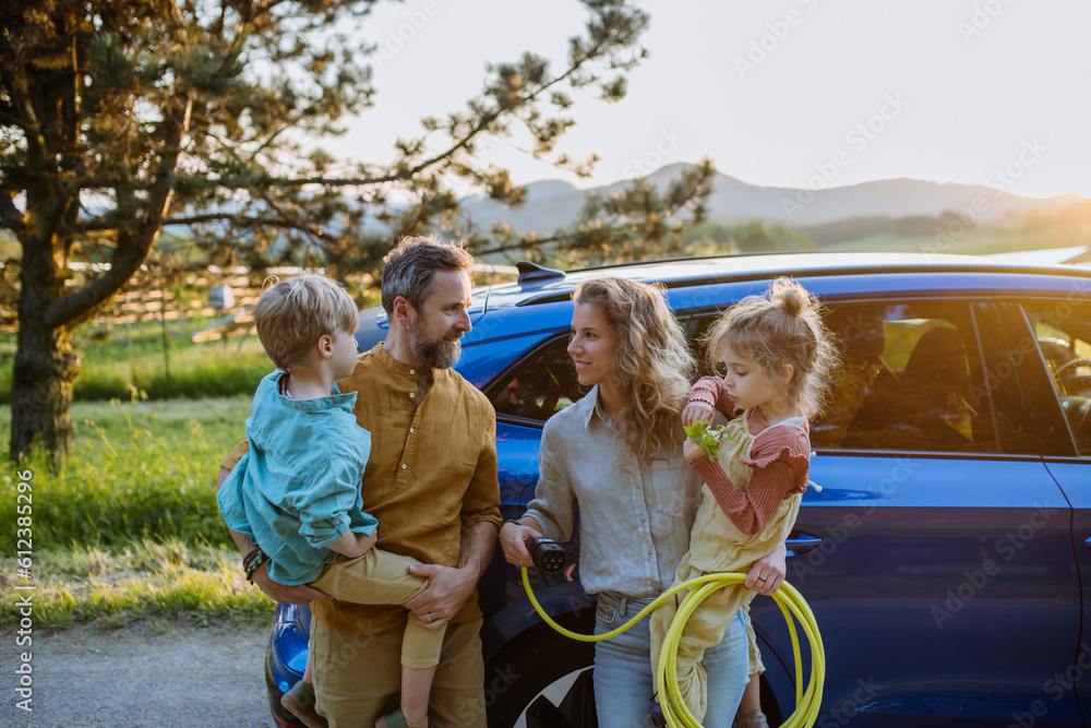 Wall mural Happy family in front of their electric car, concept of green energy and sustainable lifestyle.