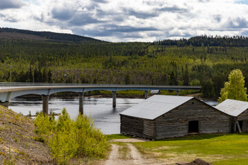 Fototapeta na wymiar Blaviksjon, Sweden A bridge over the Vindelalven river and a wooden barn.