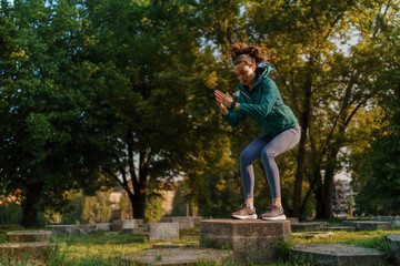 Full lenght portrait of beautiful fitness woman doing squat box jumps in the park.