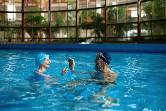 Senior man instructor teaching young woman to swim at indoor pool