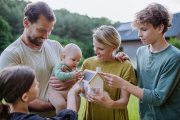 Happy family with three children holding model of house ith solar photovoltaics. Alternative...