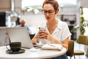 Business woman reading a text on her mobile phone while working remotely