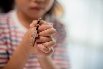 Christian concept. Little Asian girl praying withholding the cross. Concepts of hope, faith,...