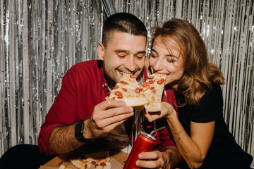 Portrait of a happy couple. They laugh, eat pizza and have a good time against the background of...