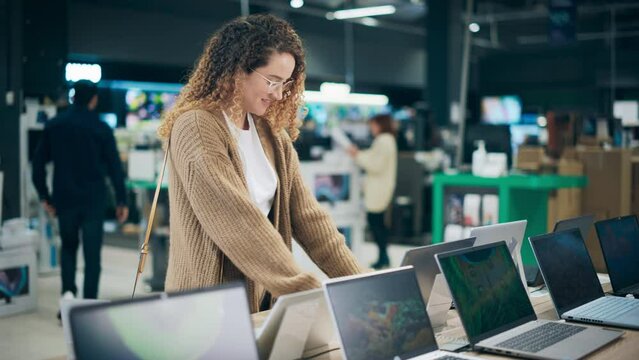 Portrait of a Stylish Female Looking at a Variety of Modern Laptops with High Quality Resolution Displays and Vivid Color Transmission. Client Shopping for a Computer in a Home Electronics Store