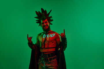 Expressive young man, rock musician, punk with neon filter on body posing against green studio...