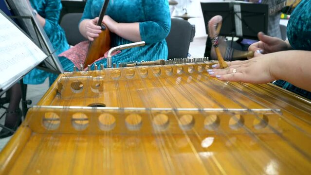 A woman plays a dulcimer with sticks.
