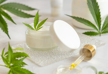 Opened white cream jar with a lid near cannabis leaves. Cosmetic Mockup