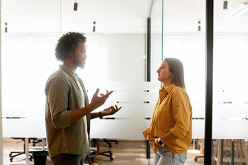 Side view at businessman standing in hallway talking to smiling businesswoman, two colleagues...