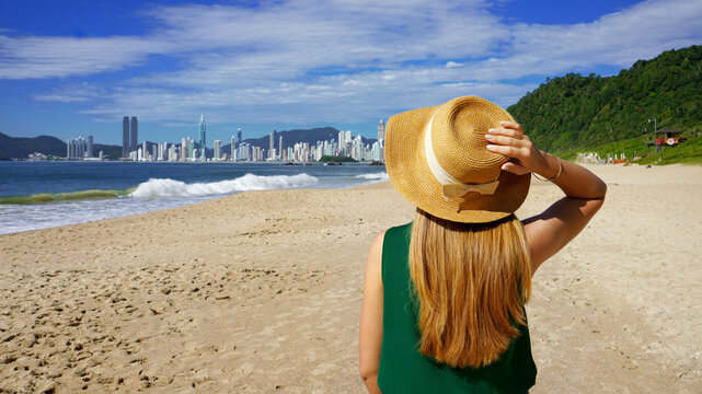 Holidays in Brazil. Panoramic view of traveler girl on Praia do Buraco beach with Balneario Camboriu skyline, Brazil.