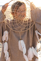 Little girl with a dream catcher on the seashore at sunset.