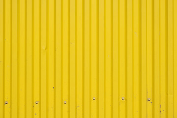 A corrugated fence of yellow metal sheets with screw