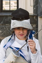 Female Fencer athlete wearing white fencing suit outfit and holding the sword, posing outdoors