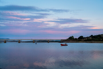 Tranquil scene with a boat on Ebro River in Asturias, Spain. Sunset colours. Tranquil water. In background is a bridge. Spectacular sunset landscape. 