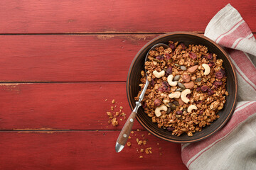 Homemade granola with greek yogurt or milk and cashews, almonds, pumpkin with dried cranberry seeds in old bowl on red rustic wooden table background. Healthy energy breakfast or snack. Top view.
