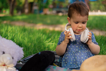 Portrait of a girl listening to music in modern headphones in a park outdoors. Happy child enjoys the rhythms of listening to music in wireless headphones