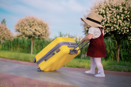 A little joyful cute girl in a blue summer dress and a straw hat holds a yellow suitcase. Vacation, holidays, trip to the sea, space for text, go on vacation