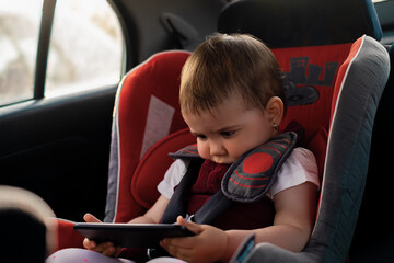 the child is sitting in a car seat, holding a mobile phone in his hands, watching cartoons on the...
