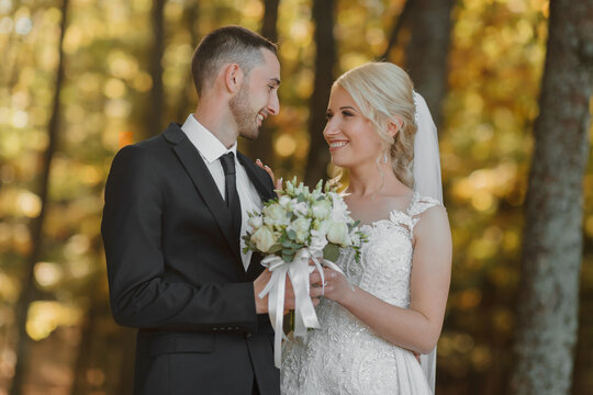 Portrait of the bride and groom in nature. Full size photo. The bride and groom are posing, hugging and smiling, against the background of the autumn forest. The bride in a long dress.