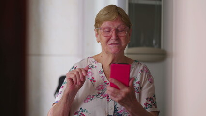 Candid senior woman waving hello to family member speaking on video conference at home. Authentic elderly lady talking to relatives looking at smartphone device screen
