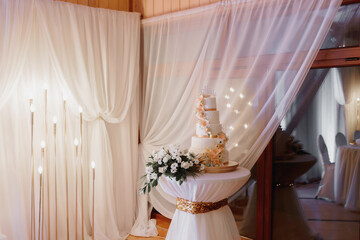 A white wedding cake, decorated with flowers and gold, stands on a glass stand. Fresh flowers at the wedding. sweets