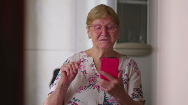 Candid senior woman waving hello to family member speaking on video conference at home. Authentic elderly lady talking to relatives looking at smartphone device screen