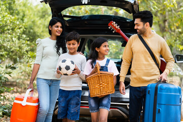 Happy indian fmaily with kids with picnic basket and travel lagguage at destination - concept safe...