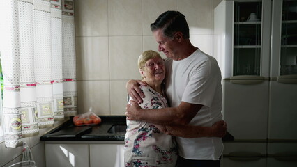 Adult son embracing elderly mother standing at home kitchen. Authentic real people lifestyle. Man...