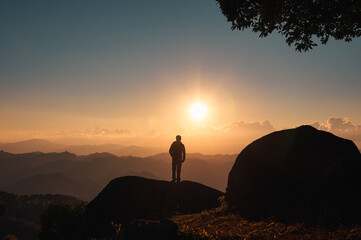 Silhouette hiker man standing on top of mountain with the sun shining over mountain in the sunset