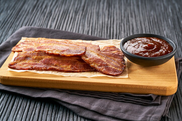 fried bacon rashers and bbq sauce on a black table, selective focus.
