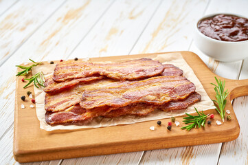 fried bacon rashers and bbq sauce on a white table, selective focus.