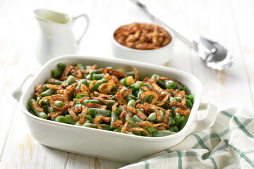 green bean casserole with crispy fried shallots and cream sauce on a white wooden table.