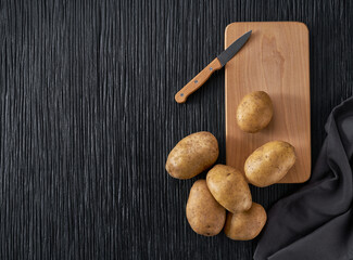 Fresh potato tubers on a black wooden table, top view.