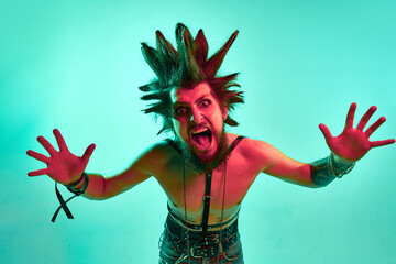 Portrait of young crazy looking man, punk with expressive hairstyle posing shirtless against blue...
