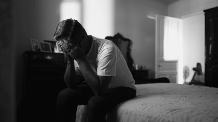 Older man suffering in quiet despair struggling with mental problems in home bedroom in monochrome black and white